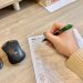 Hands reviewing and filling property verification paperwork at a desk