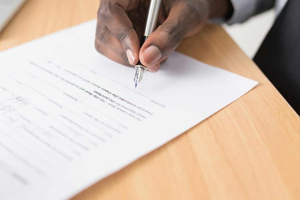 Hands signing a property document with a pen while verifying land title paperwork in Nigeria