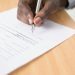 Hands signing a property document with a pen while verifying land title paperwork in Nigeria