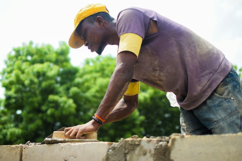 A Nigerian bricklayer laying blocks on a wall, illustrating how to vet a qualified builder and avoid quacks in Nigeria in 2026