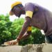 A Nigerian bricklayer laying blocks on a wall, illustrating how to vet a qualified builder and avoid quacks in Nigeria in 2026
